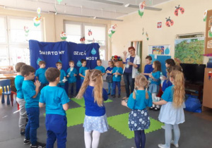 Dzieci stojąc z nauczycielką w kole trzymają puste butelki plastikowe podczas zabawy dźwiękonaśladowczej.